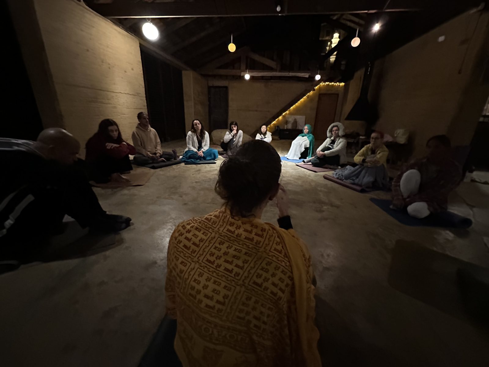 Grupo de alunos reunido em círculo no salão à luz de velas durante o satsang noturno